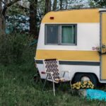 Image of a small vintage RV in a field of grass against a backdrop of trees.